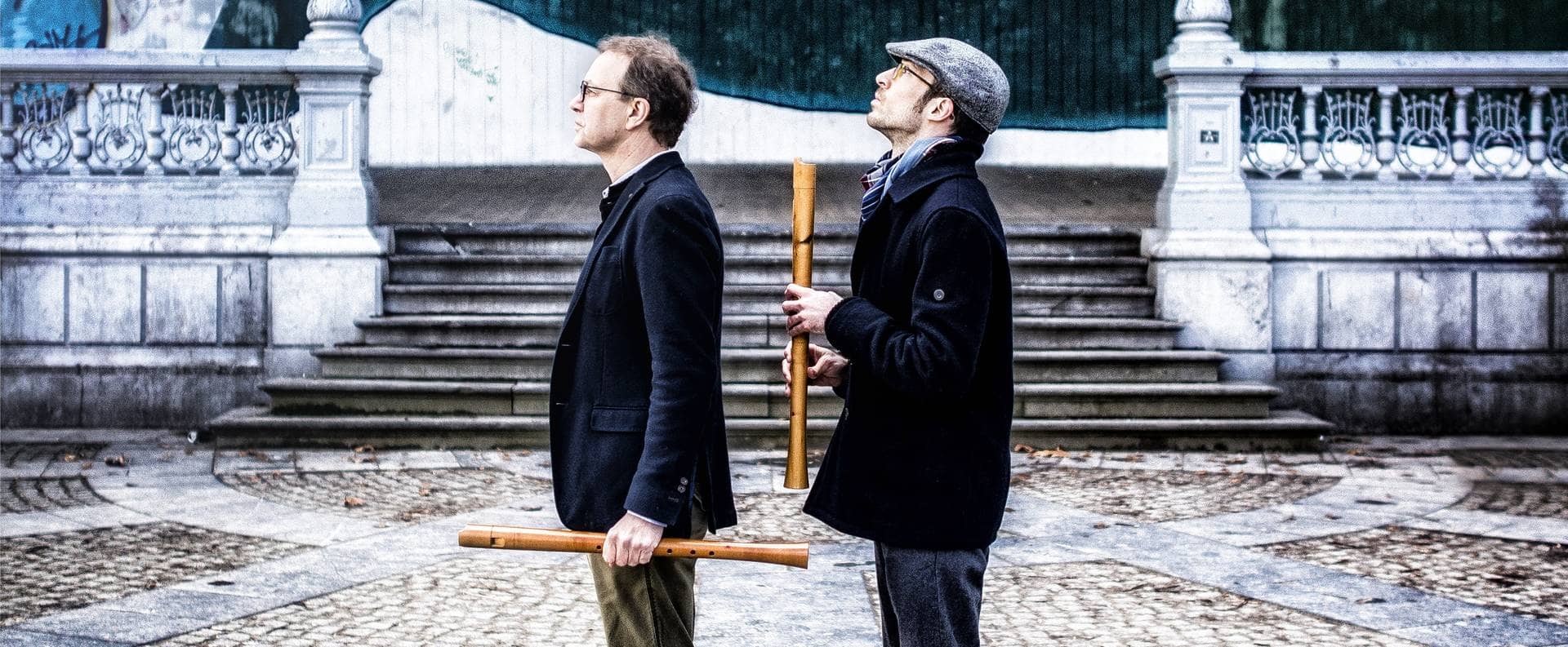 Zwei Männer stehen mit Blockflöten in der Hand vor einer Veranda