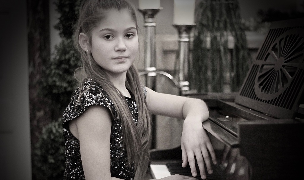 Mädchen sitz am Klavier und schaut in die Kamera