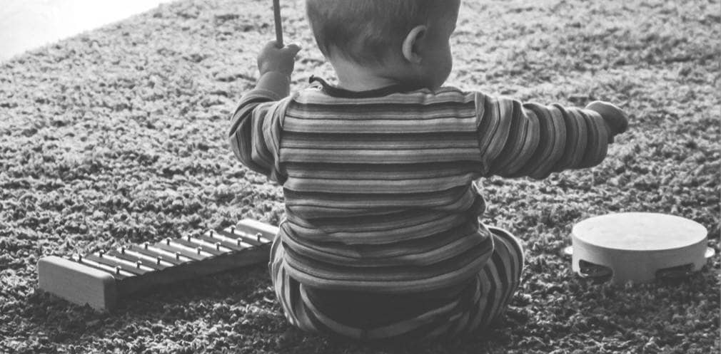 Kind sitzt auf einem Teppich und spielt auf einem Glockenspiel